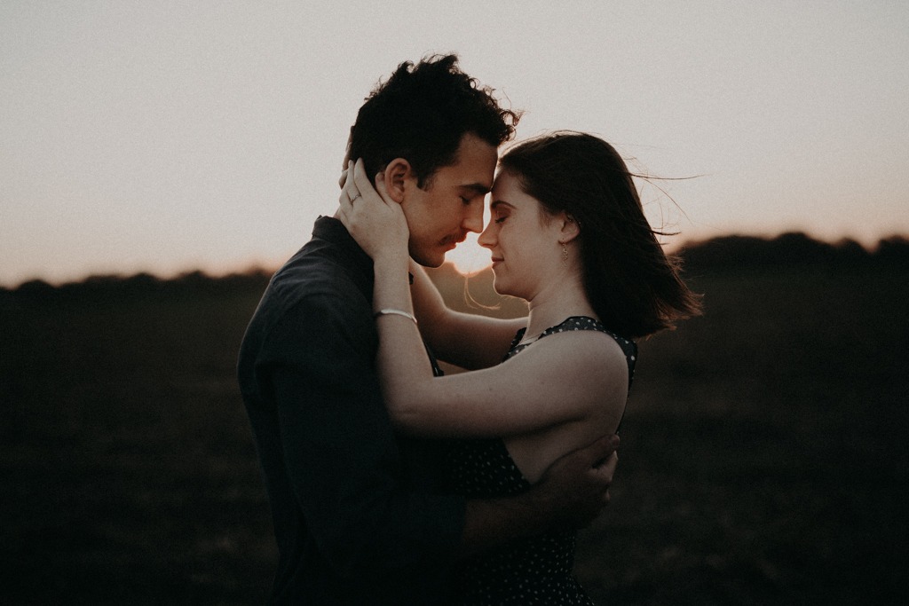 Man and woman hugging in field at sunset